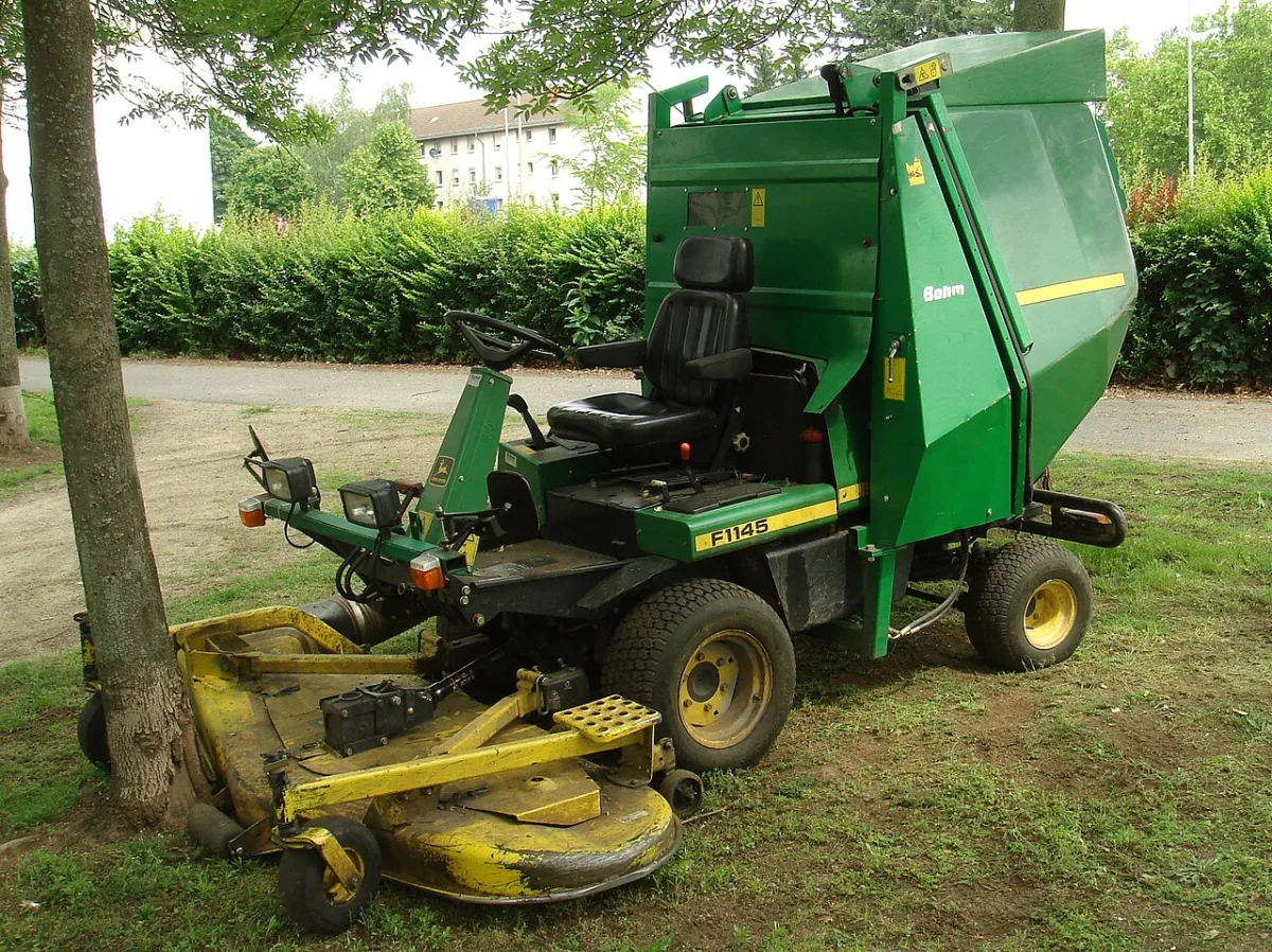 Groene zitgrasmaaier met opvangbak en maaidek, geparkeerd op gras naast een boom
