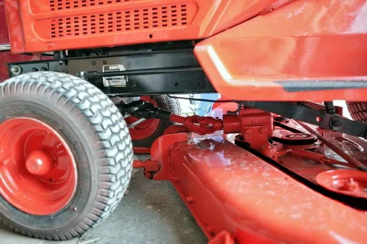 Close-up van een aandrijfas en maaidek onder een Kubota zitgrasmaaier